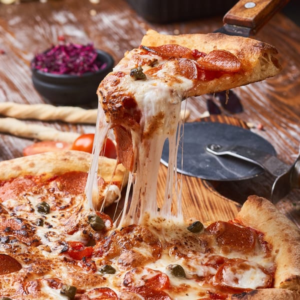 A slice of Tony's Pizzeria pepperoni and mushroom pizza with melted cheese being lifted from the pie.