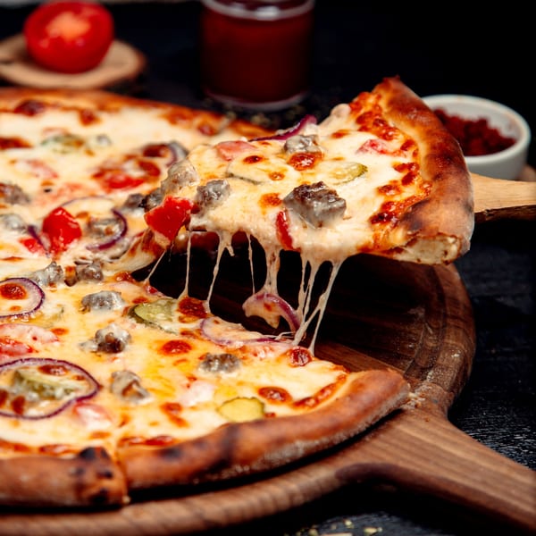 A slice of Tony's Pizzeria pizza with melted cheese, sausage, red onion, and peppers being lifted.