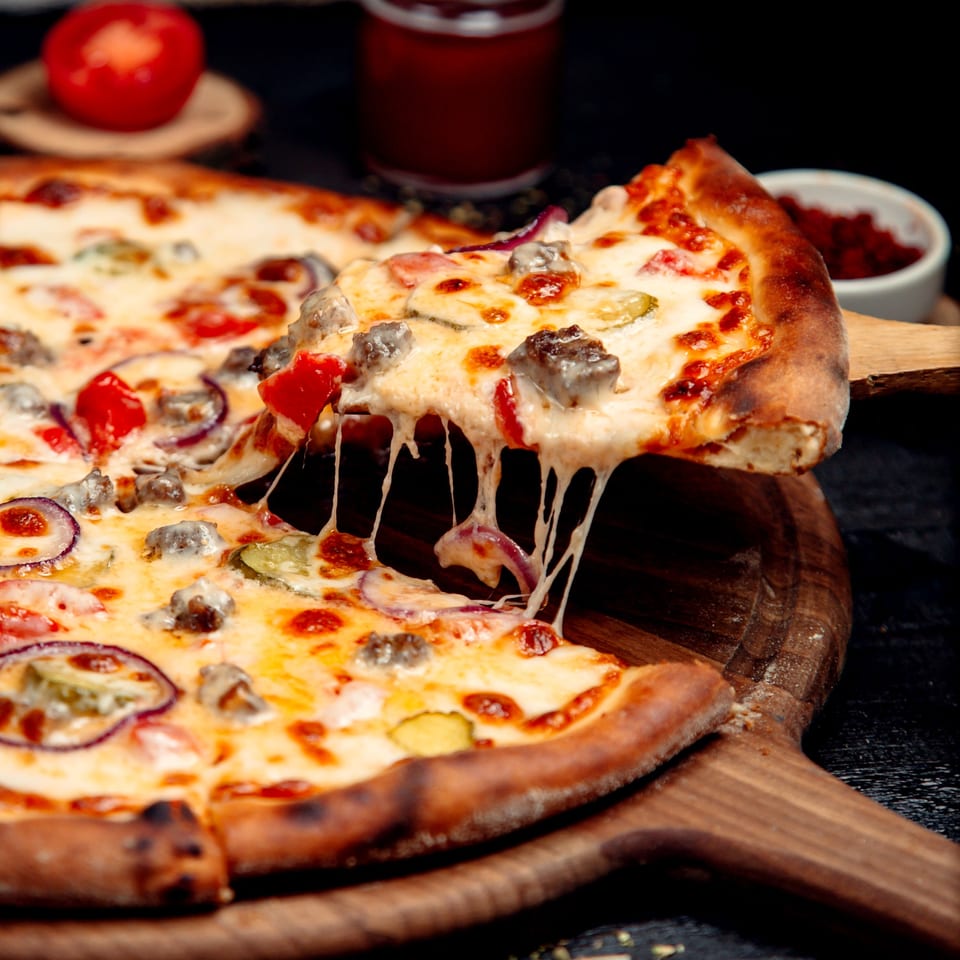 A slice of Tony's Pizzeria pizza with melted cheese, sausage, red onion, and peppers being lifted.