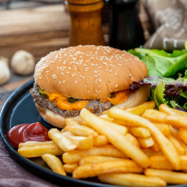 Cheeseburger with fries, ketchup, and a side salad on a black plate.