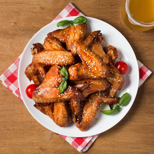 Plate of Tony's Pizzeria chicken wings with sesame seeds, basil, and cherry tomatoes, with a beer.